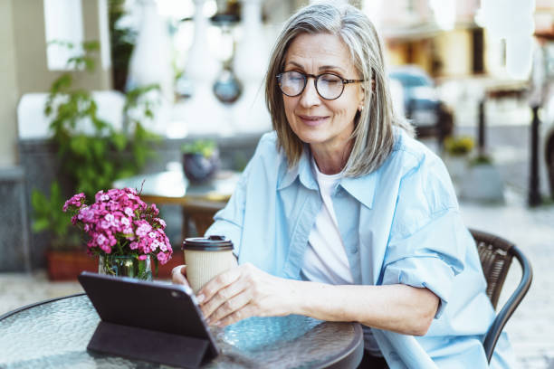 istock Mature lady enjoying outdoors while searching for information on tablet PC. Woman seated at cafe table on street, sipping cup of coffee. Moment of leisure and relaxation. 1714802644