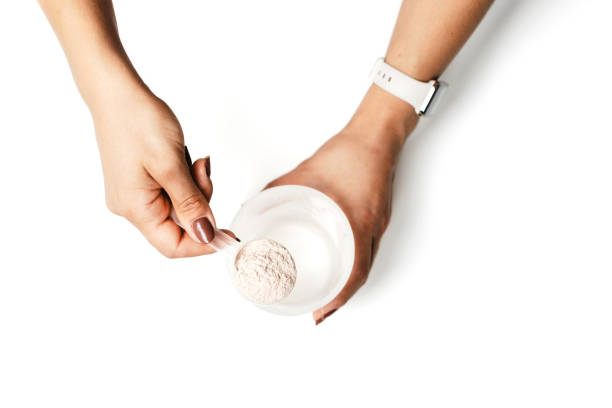 istock Woman's hands with measuring spoon puts portion of whey protein powder into a shaker, making protein drink cocktail, isolated on white background, top view 1714810093