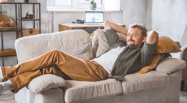 Photo of Man enjoying peaceful moment home, laying comfortably on sofa. Concept of freelancing and working from home, which has become increasingly popular in recent years. Handsome spent time home.