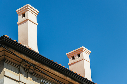 Amidst the contrasting shadows and abstract rooftop, two chimneys punctuate the vibrant blue sky