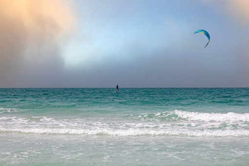 Carefree man having fun while jumping high-up with kiteboard during summer day at sea.