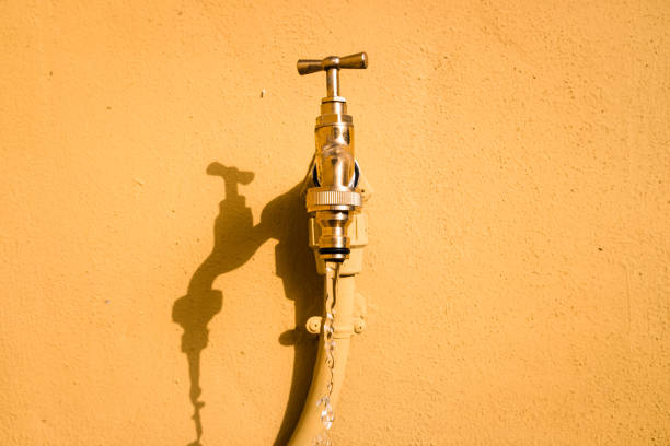 A wall tap on a wall in the sun from which fresh water drips.