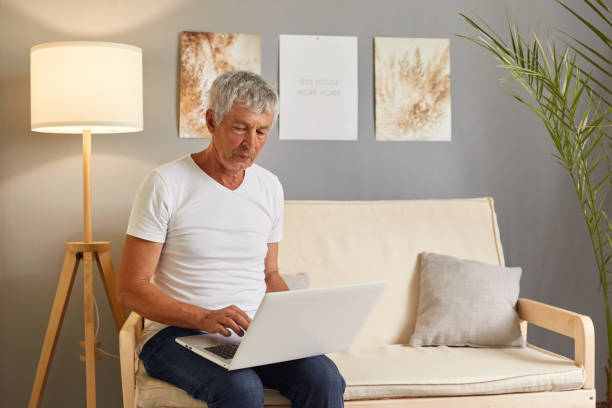 istock Concentrated focused mature man sitting on couch using modern laptop easy technology usage, senior male working on computer looking at laptop screen. 1714869663