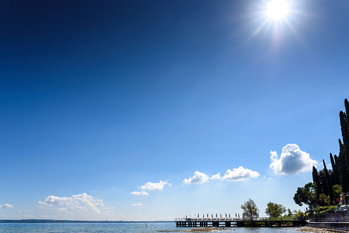 A strong sun illuminates the lake on a clear summer day, with space for text in the blue sky.