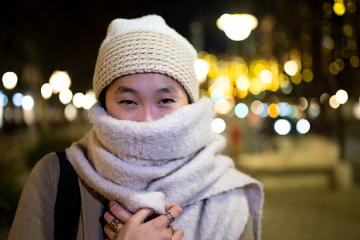 Beautiful young girl wearing knitted hat and scarf at night. Young woman looking at camera during winter standing outside.