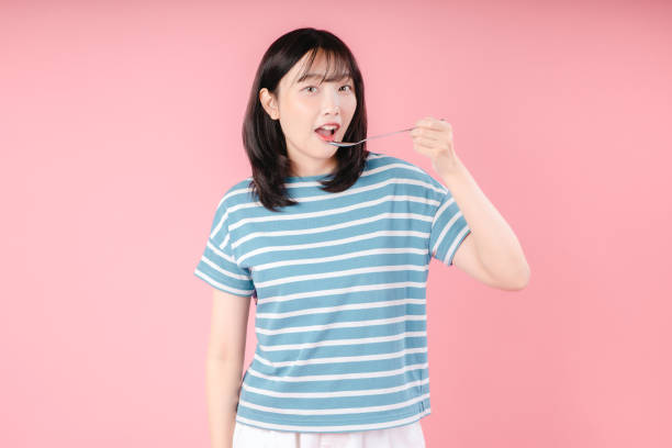 mujer joven atractiva comiendo comida sabrosa sobre fondo rosa - women spoon tasting elegance fotografías e imágenes de stock