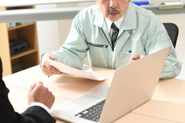 A businessman in a suit explaining on a laptop and a middle-aged man in work clothes listening to the explanation.