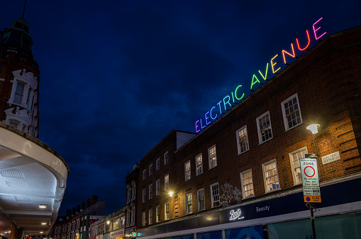 Brixton, London, UK: Electric Avenue in Brixton at night. Seen from Brixton Road with the colorful Electric Avenue neon sign.