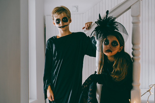 Teenagers dressed in halloween costumes sitting on the stairs on a Halloween party at home