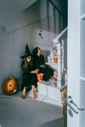 Teenagers dressed in halloween costumes sitting on the stairs on a Halloween party at home