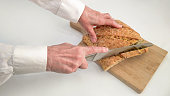 Senior Female Hands Cutting Integral Whole Grain Bread Loaf With Large Stainless Steel Knife On Wooden Chopping Board High Resolution Stock Photo