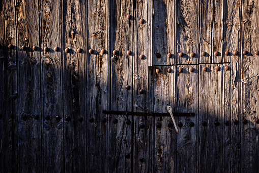 Old and decrepit wooden gate, half lit by the sun, in an unpopulated rural area.