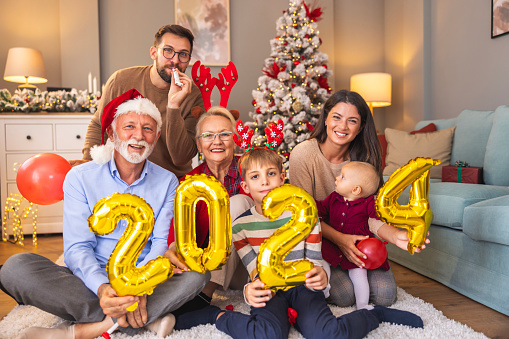 Beautiful happy family celebrating Christmas at home, having fun holding giant balloons shaped as numbers 2024, representing the upcoming New Year