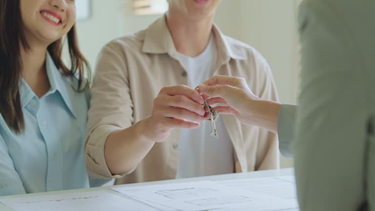 Happy married asian couple receiving the house key from female real estate agent after buying the first new house property agreement successful deal