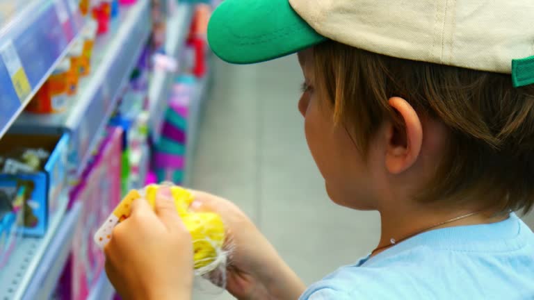 Close-up of a cute boy taking a rubber toy from the plastic basket in a toy store and examining it