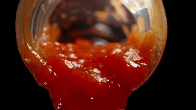 From the bottle, ketchup is slowly dripping, against a black background, with a macro zoom.