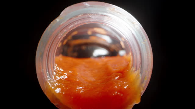 Ketchup is pouring out of the bottle as the camera emerges from the inside. Dolly slider extreme close-up.