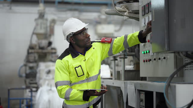 Engineer holding a digital tablet is checking the operation of a plastic machine.