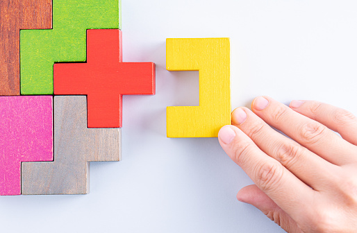 Hand holding wooden puzzle element. Hand sets the last element of the puzzle. The concept of logical thinking. Geometric shapes on a wooden background. Wooden blocks.