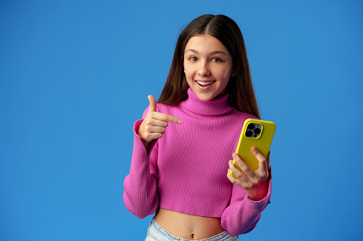 Stylish teen girl using smartphone over blue background in studio