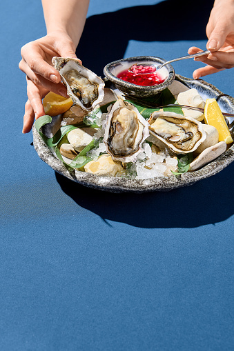 Vertical side view of a woman's hand picking up a fresh oyster, a luxury dining moment captured