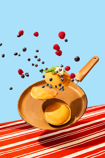Food pop art photography. Close up. Flying frying pan with hot, sweet, delicious pancakes with berries. Vintage, retro 80s, 70s style, interior. Complementary colors. Concept of food, cooking. Ad