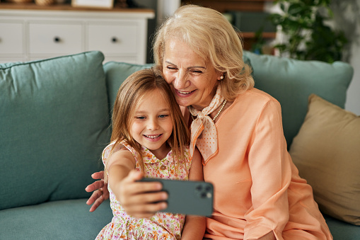 Happy grandmother and granddaughter taking selfie at home