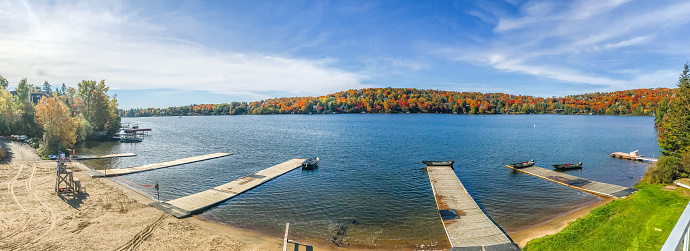 Beach and lake of Lac Beauport during autumn day where we see small pier in foreground and colorful tree mountain in background