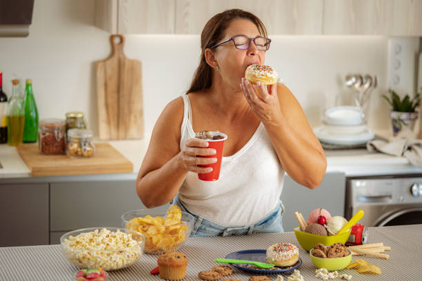 femme gourmande qui aime manger un beignet et boire du cola. concept d’alimentation malsaine - avoir faim photos et images de collection