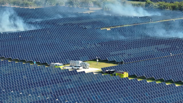 Aerial view of fire burning at big sustainable electric power plant with many rows of solar photovoltaic panels for producing clean electrical energy. Seasonal wildfire at critical infrastructure