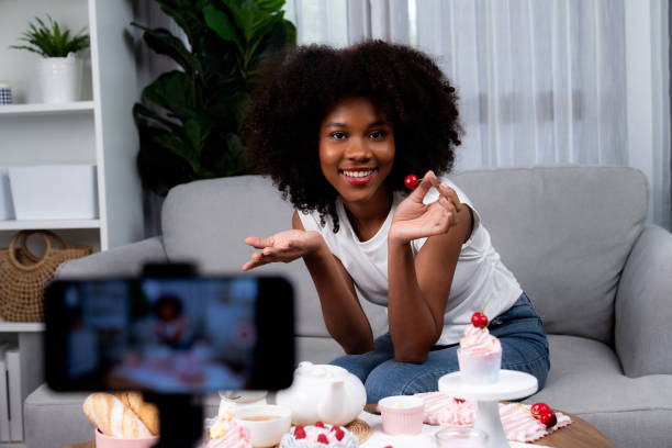 istock Young African presenting cupcake with video record on smartphone. Tastemaker. 1715072962