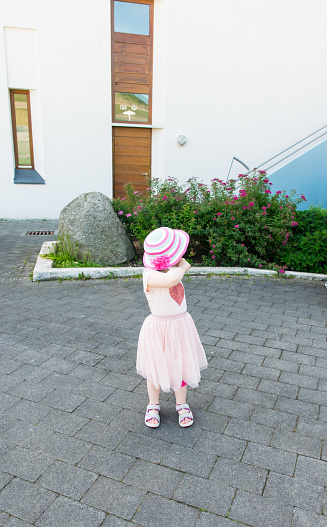 The little girl in a pink dress and a hat walks on the summer city and is photographed at the moment when she turned back