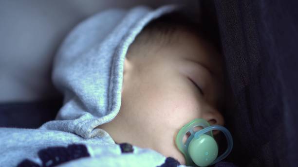 A little boy sleeps in a stroller close-up. Child with a pacifier.