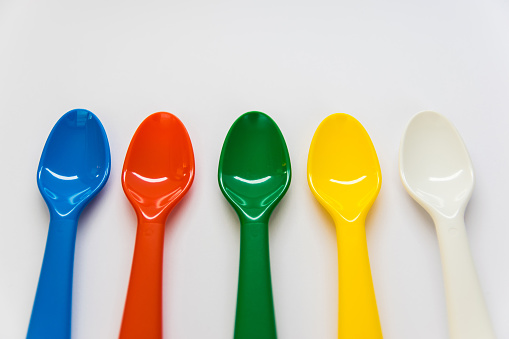 Multicolor plastic spoons on the white background. White, yellow, green, red, blue spoons can be used as a decorative elements or for food.