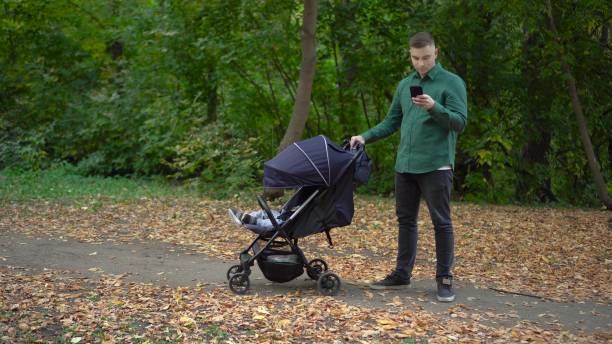 istock A young father is texting on a smartphone and rocking his child in a stroller. A man with a phone in the autumn forest. 1715078976