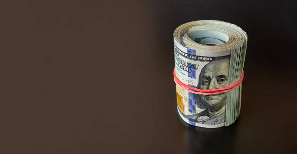istock Many hundred dollar bills rolled up with a red rubber band on a black background. 1715085895