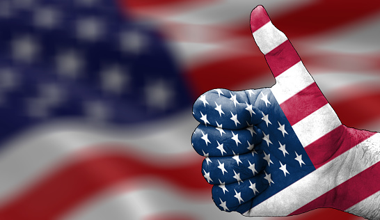 hand with thumbs up in approval with the America USA flag painted. Image with America USA flag background area out of focus, copy space area