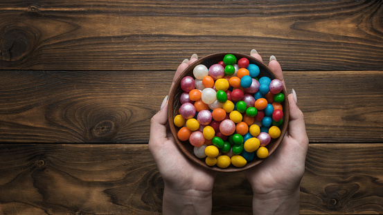 A bowl with a lot of sweets in the hands of a girl on a wooden background. Sweet treat.