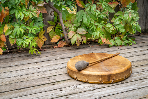 handmade, native American style, shaman frame drum covered by goat skin with a beater on a rustic wooden backyard deck