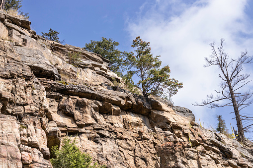 Sedimentary rock on mountain cliff topped with trees with blue sky