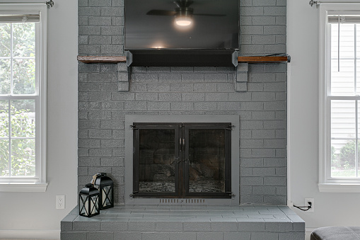 Grey Brick Fireplace with TV Hung on Wall and Two Candle Light Farmhouse Lanterns and Sunny Windows