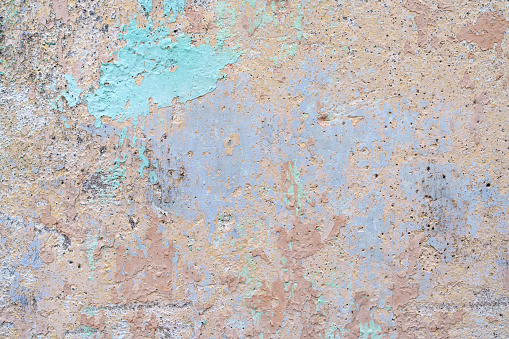 Flaking turquoise blue paint on the stucco exterior wall of an old house