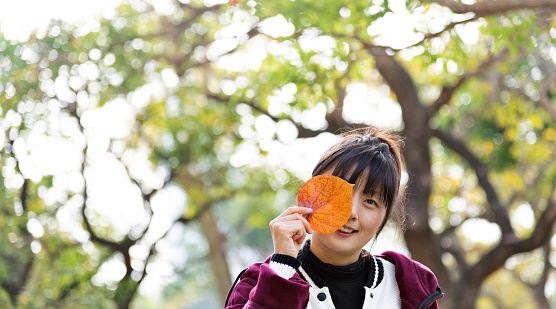 Woman covering eye with hibiscus leaf in autumn.