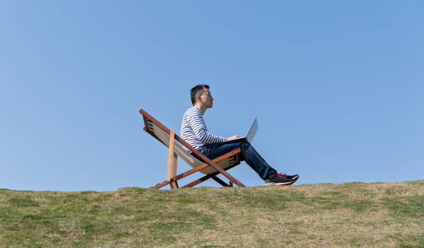 istock Man sitting on deck chair and using laptop 1715175519