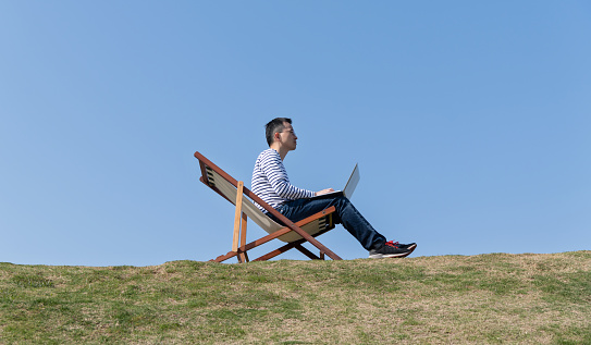 Man sitting on deck chair and using laptop.