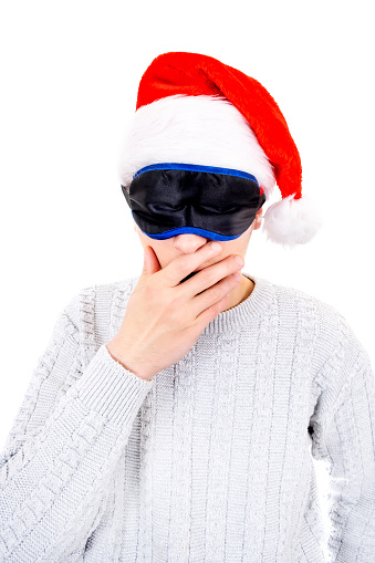 Young Man in Santa Hat and Sleep Mask is Yawning Isolated on the White Background