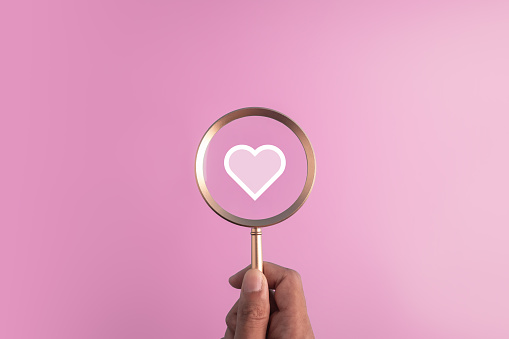 find love concept for Valentine day,marriage and romantic moment.red heart icon and hand holding the magnifier glass on pink background.