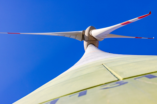 Rotor with nacelle and blades of a wind turbine with tall tower seen from below against blue sky