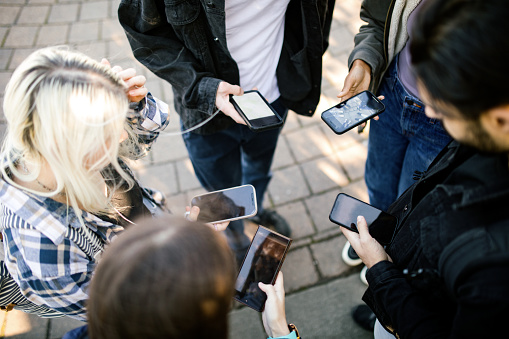 A group of multiracial young adults use their phones to share information, browse the internet, and engage with social media.  Technology content concept.