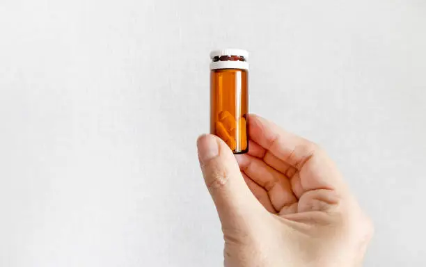 Person hold a Pills in Vial on the White Wall Background closeup